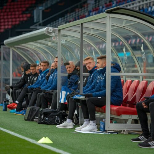 Ersatzbank mit Spielern und Betreuern hinter Plexiglas im Fußballstadion