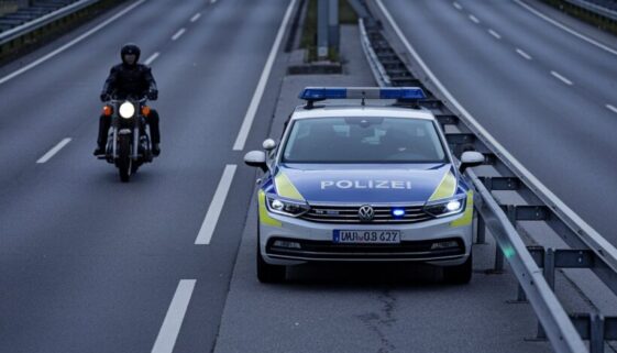Polizeiauto auf der Autobahn, Motorradfahrer in Lederkleidung fährt auf der linken Spur.