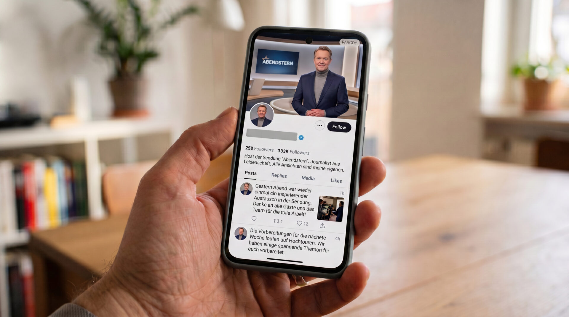 Nahaufnahme eines Smartphones mit einem täuschend echten Fake-Profil eines Moderators in einer Hand.