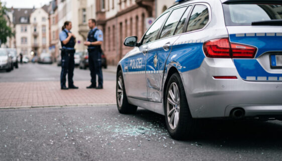 Defektes Polizeifahrzeug mit Dellen an der Seitenwand liegt auf einer normalen Stadtstraße, Glassplitter am Asphalt.